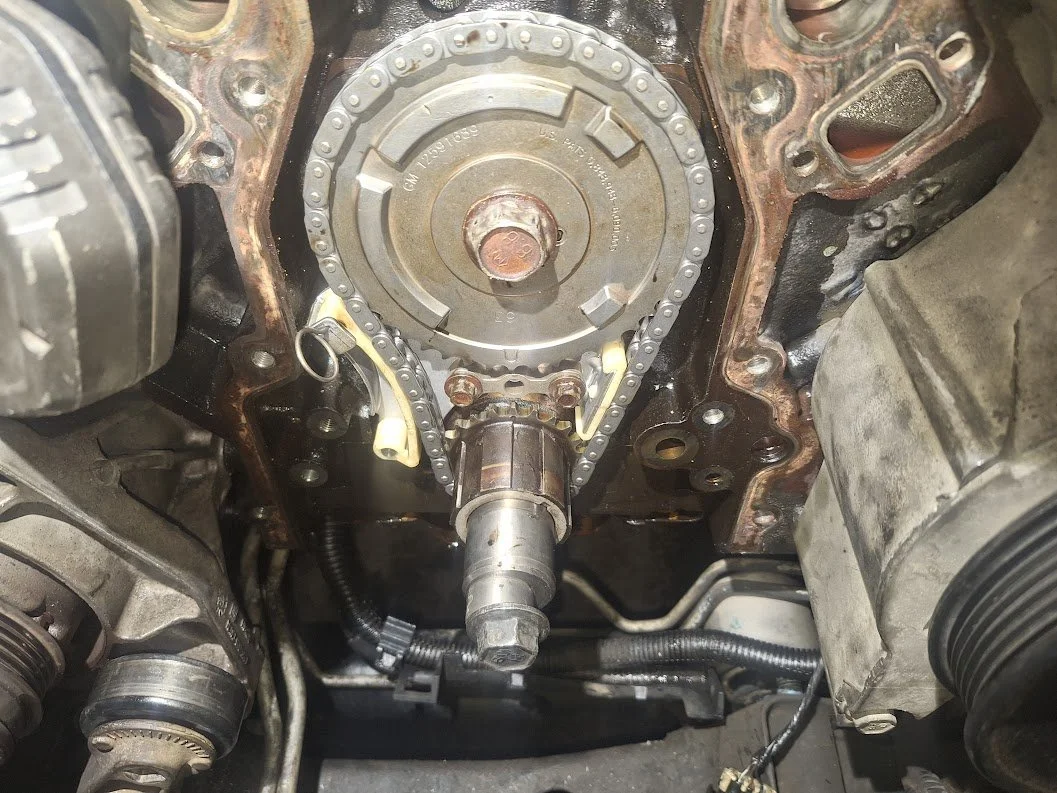 Close-up view of a car engine's timing chain and sprockets, with parts removed for maintenance.