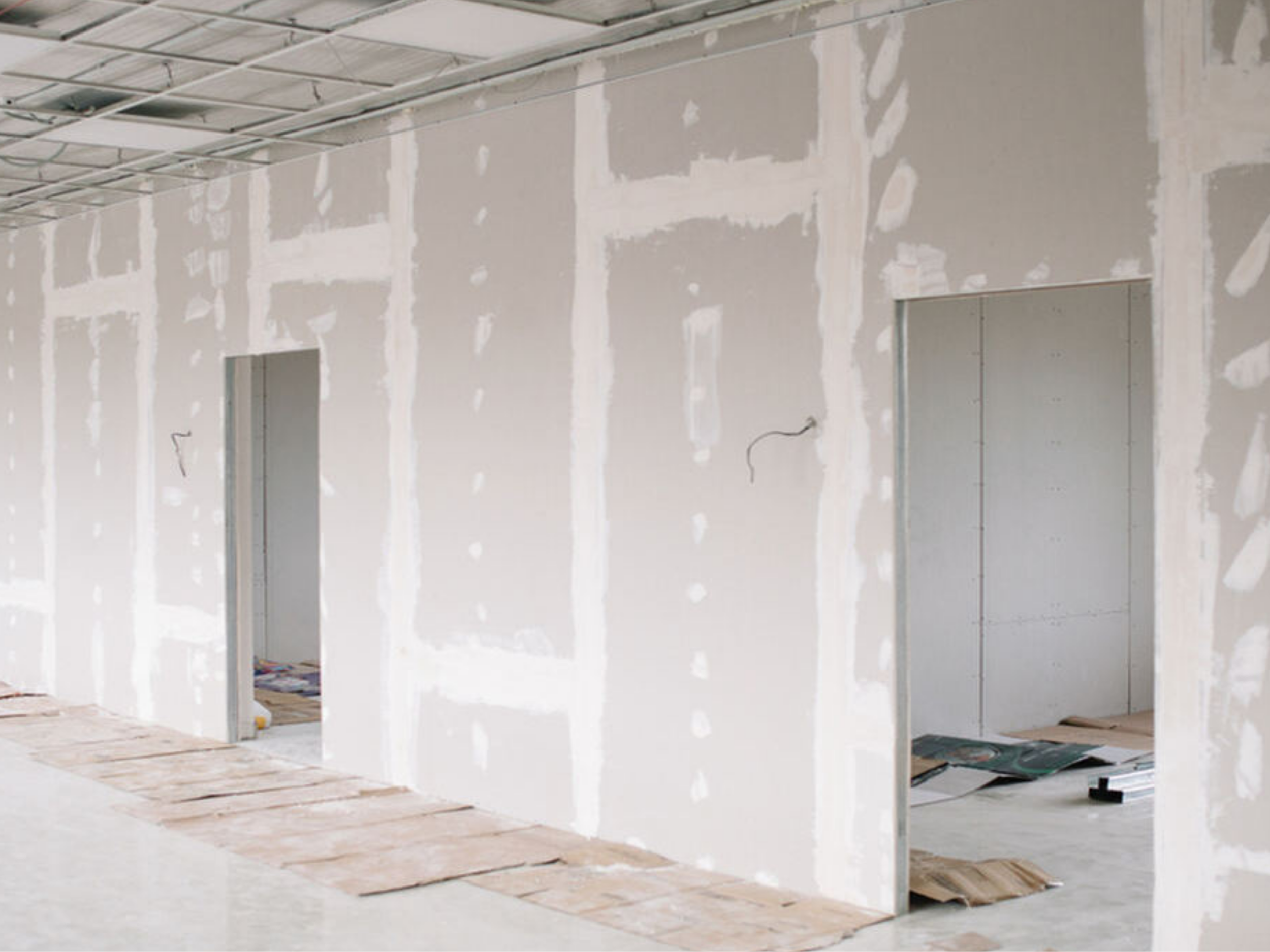 Interior view of a building under construction with drywall unfinished walls and doorways, scattered construction materials on the floor.