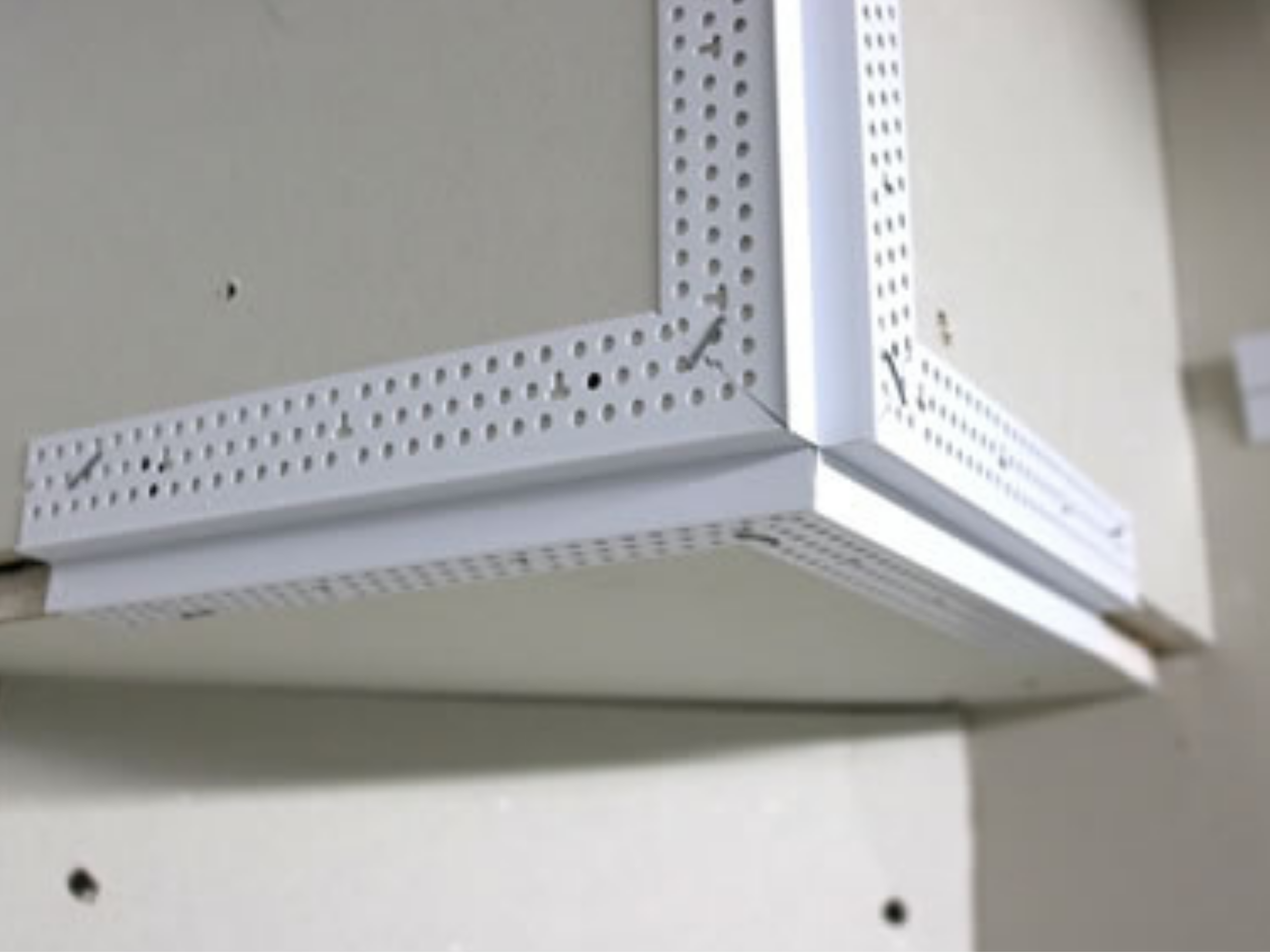 Close-up of a white metal pegboard corner bracket attached to a wall.
