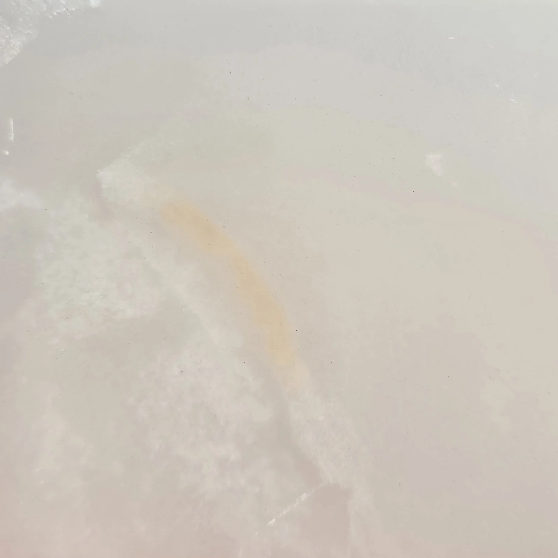 Close-up of a white Onyx natural stone with a faint orange streak and some specks.