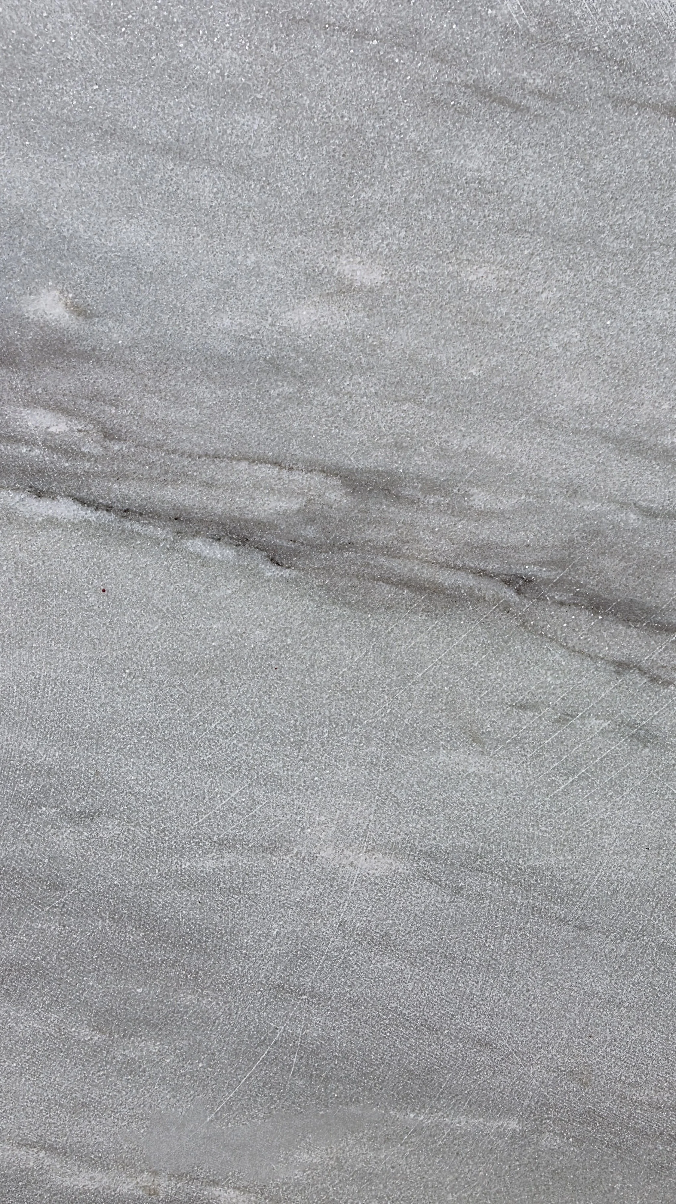 Close-up of a textured surface that appears to be sand or fine gravel with a grayish tone and a natural, slightly uneven pattern.