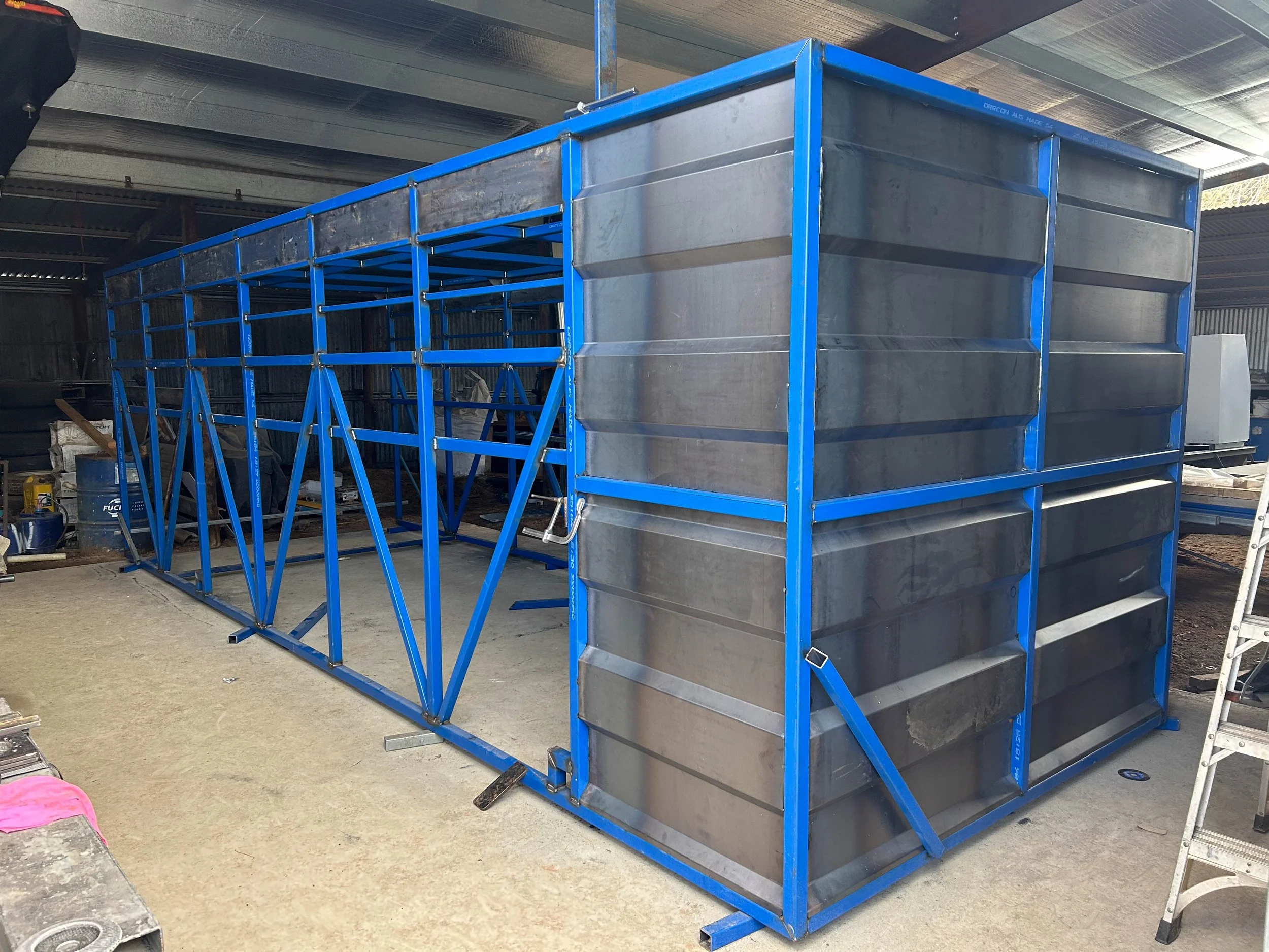 Inside an unfinished industrial warehouse with steel beams, yellow safety railings, and scaffolding. Construction equipment such as scissor lifts and a cherry picker are present, with an open loading dock area in the background.