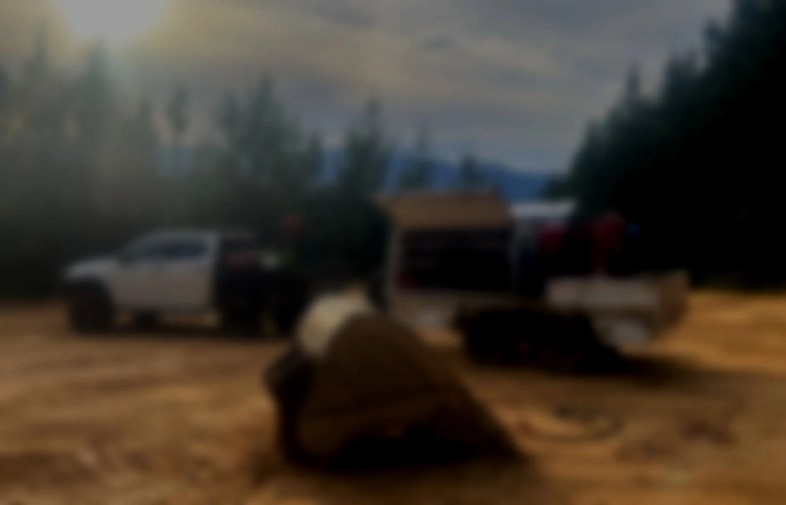 A blurry outdoor scene with a white and black pickup truck, a white trailer, and some trees in the background.