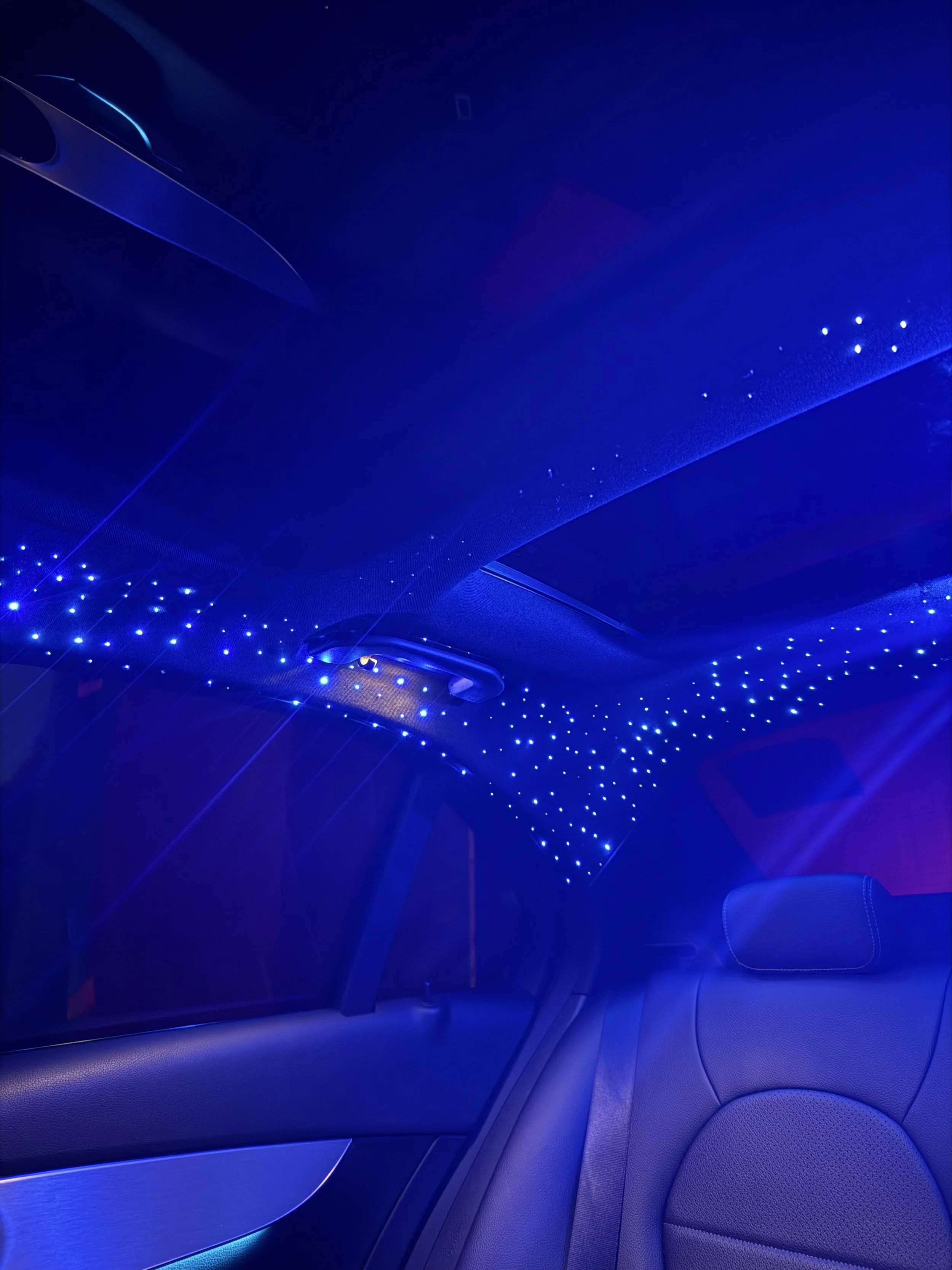 Inside a car with blue starry LED ceiling lights and dark leather seats.