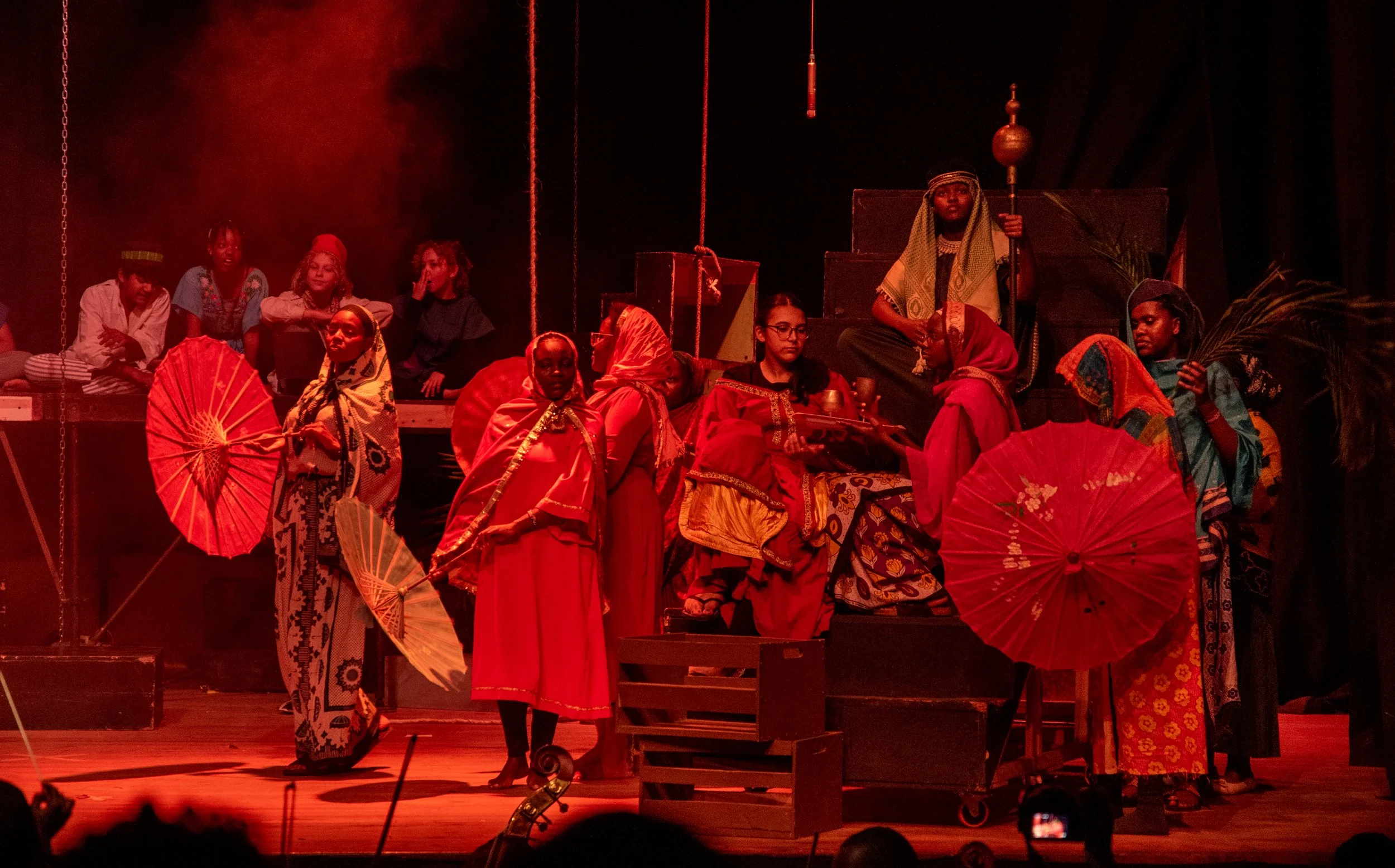 Theater stage with performers in colorful costumes, holding umbrellas, in a scene inspired by African culture.