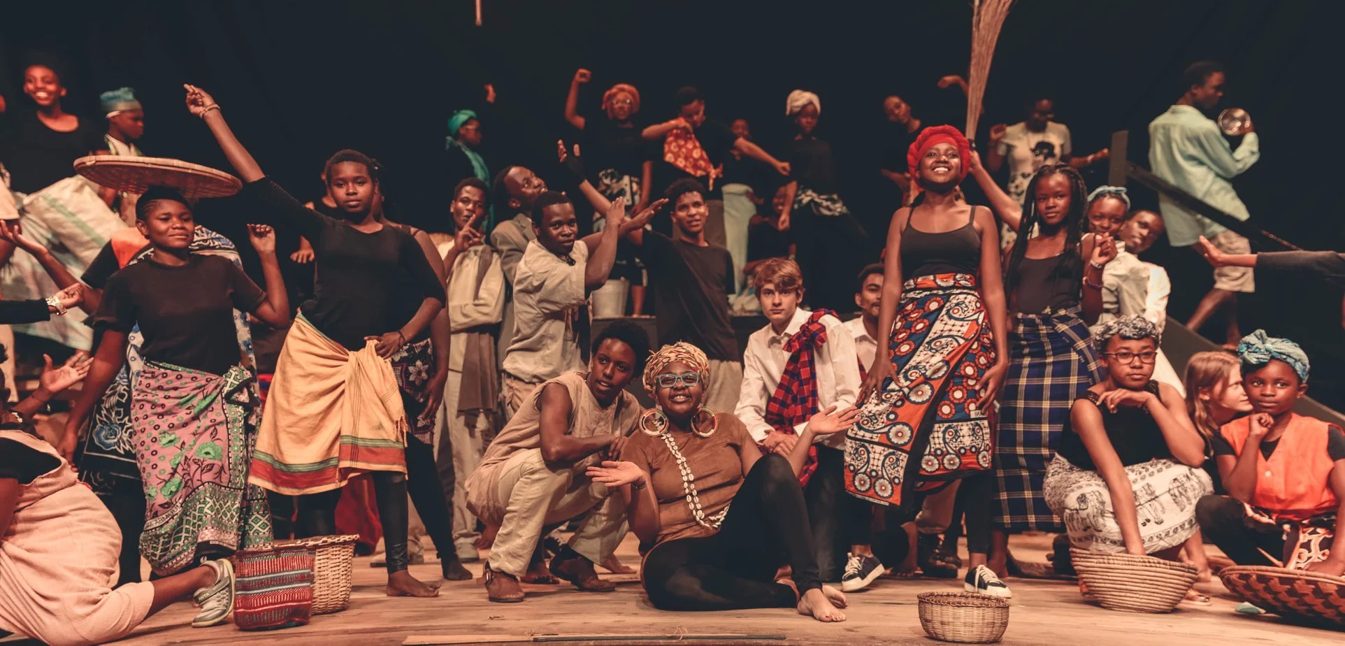 Group of diverse children and adults on stage, dressed in traditional and casual clothing, participating in a cultural performance or celebration.