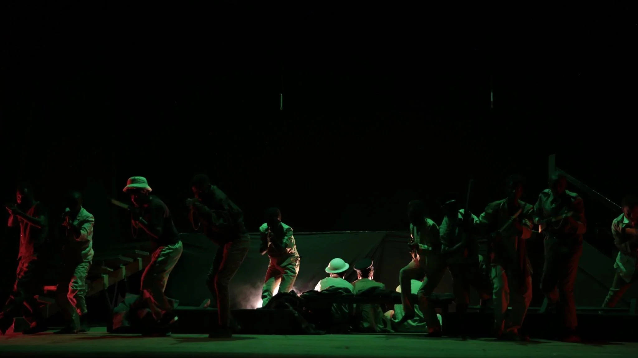 People performing on stage at night, with some sitting and others standing, illuminated by green light.