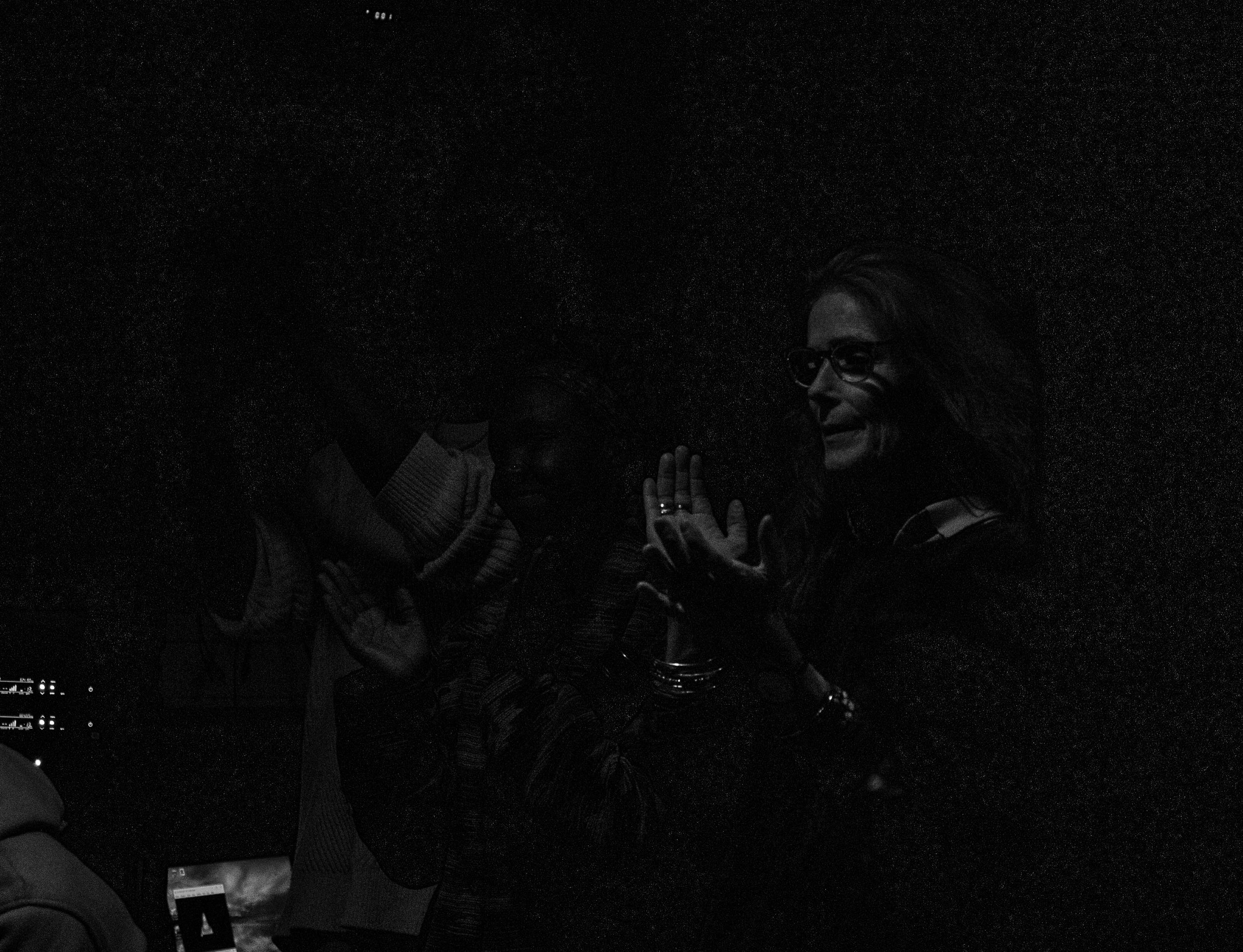 Two people engage in a conversation at night; one appears to be smiling with glasses, while the other is partially visible and facing away.