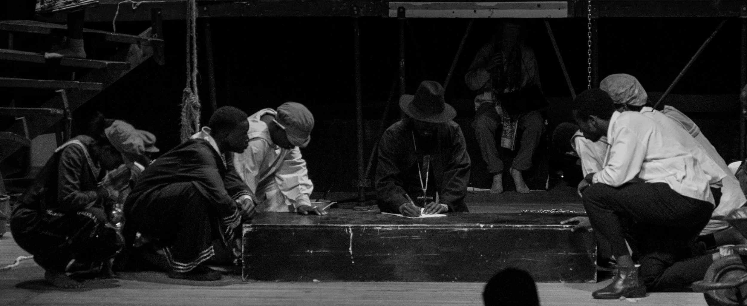 Group of people kneeling and praying on stage in a church or auditorium setting, with some bowing heads and others looking downward, in black and white.