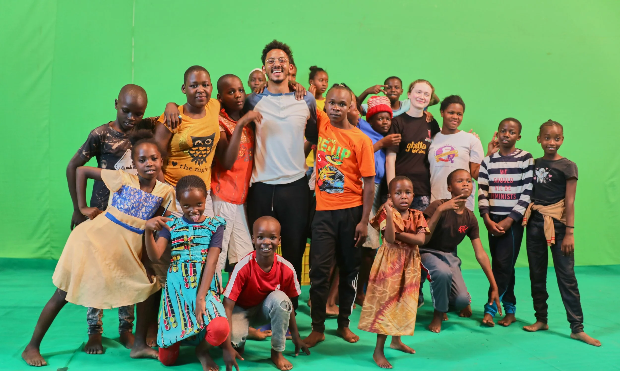 A group of diverse children and a young man standing together on a green screen background, smiling and posing for a photo.