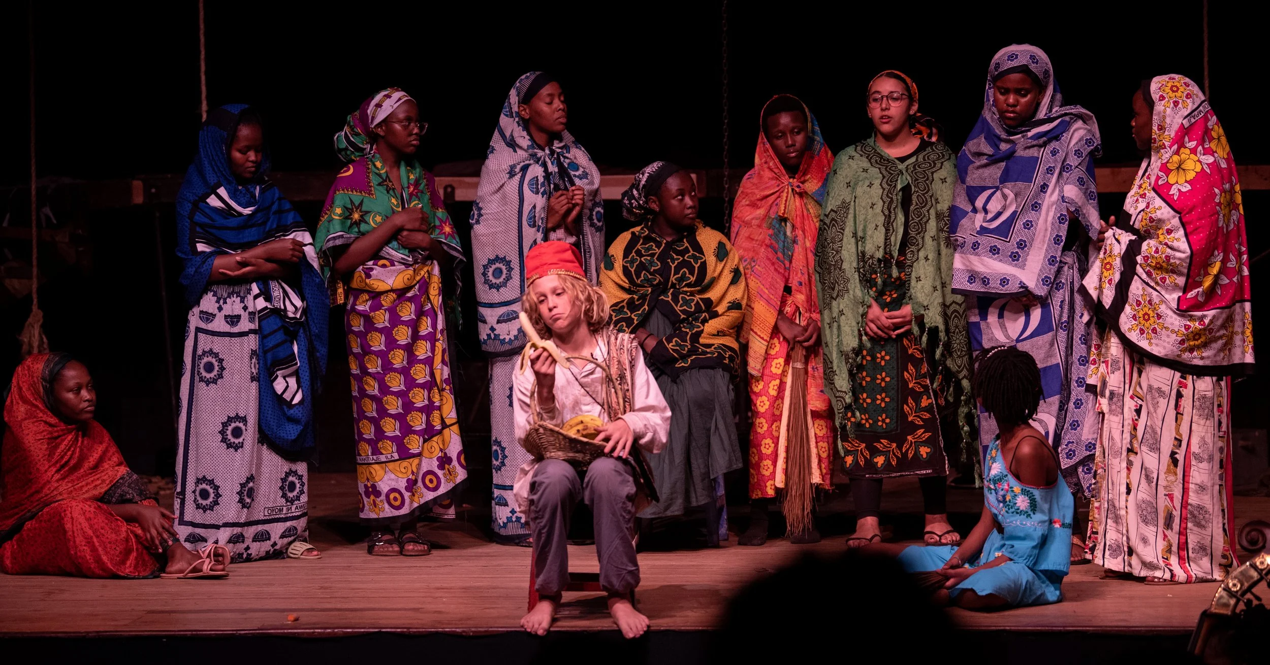 Children in colorful costumes performing on a stage for a holiday nativity scene, with some dressed as Mary, Joseph, and other biblical characters.