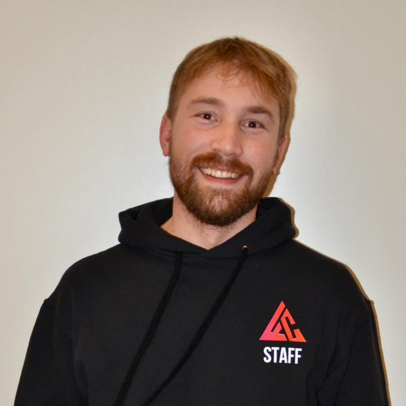 Un jeune homme souriant portant un sweat à capuche noir avec un logo rouge et blanc et le mot "STAFF"