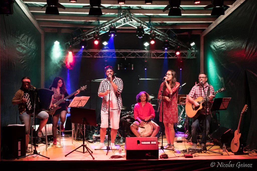 Groupe de musiciens jouant sur scène avec instruments, éclairage coloré, enregistrement live.