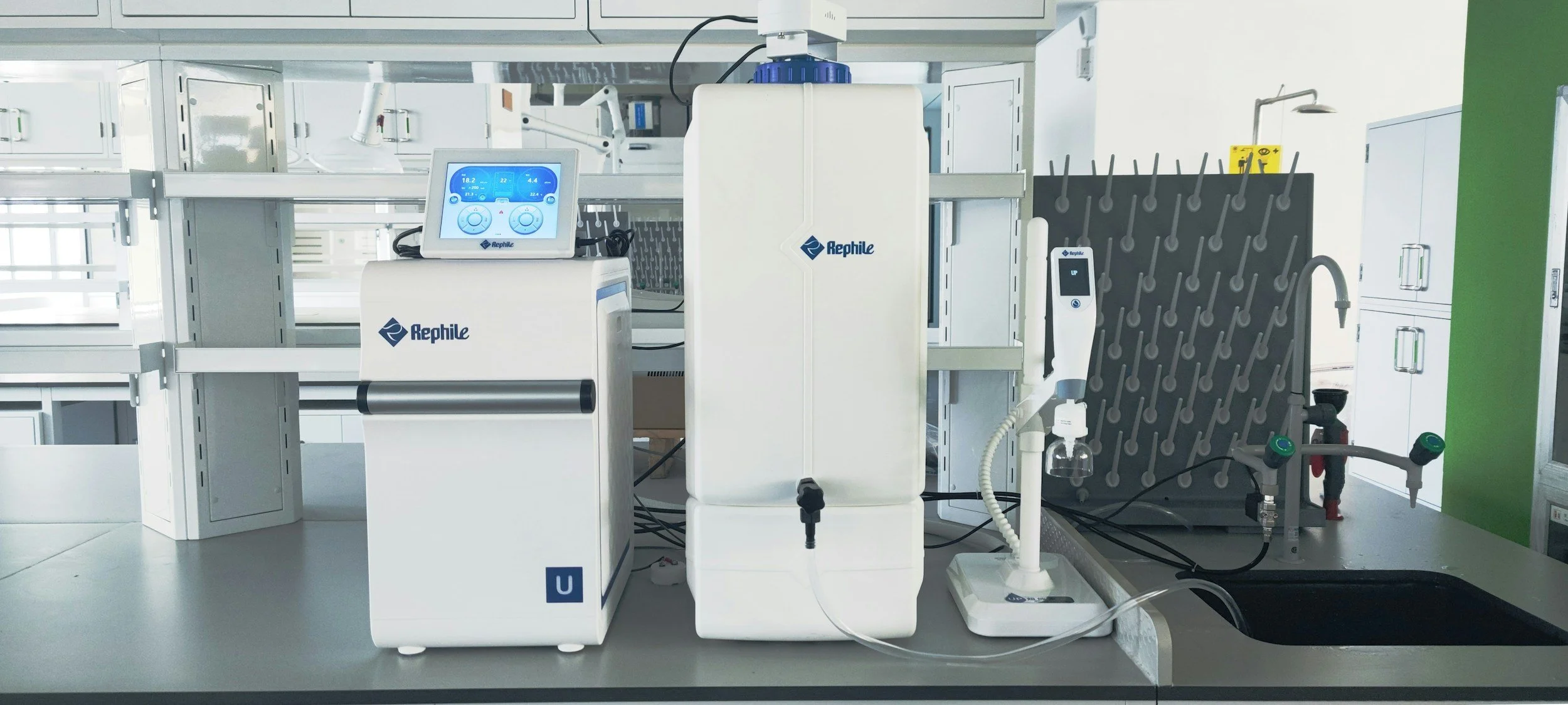 Laboratory setup with Rephile equipment including a monitor, a device with a drip mechanism, a panel with probes, and other lab instruments on a countertop.