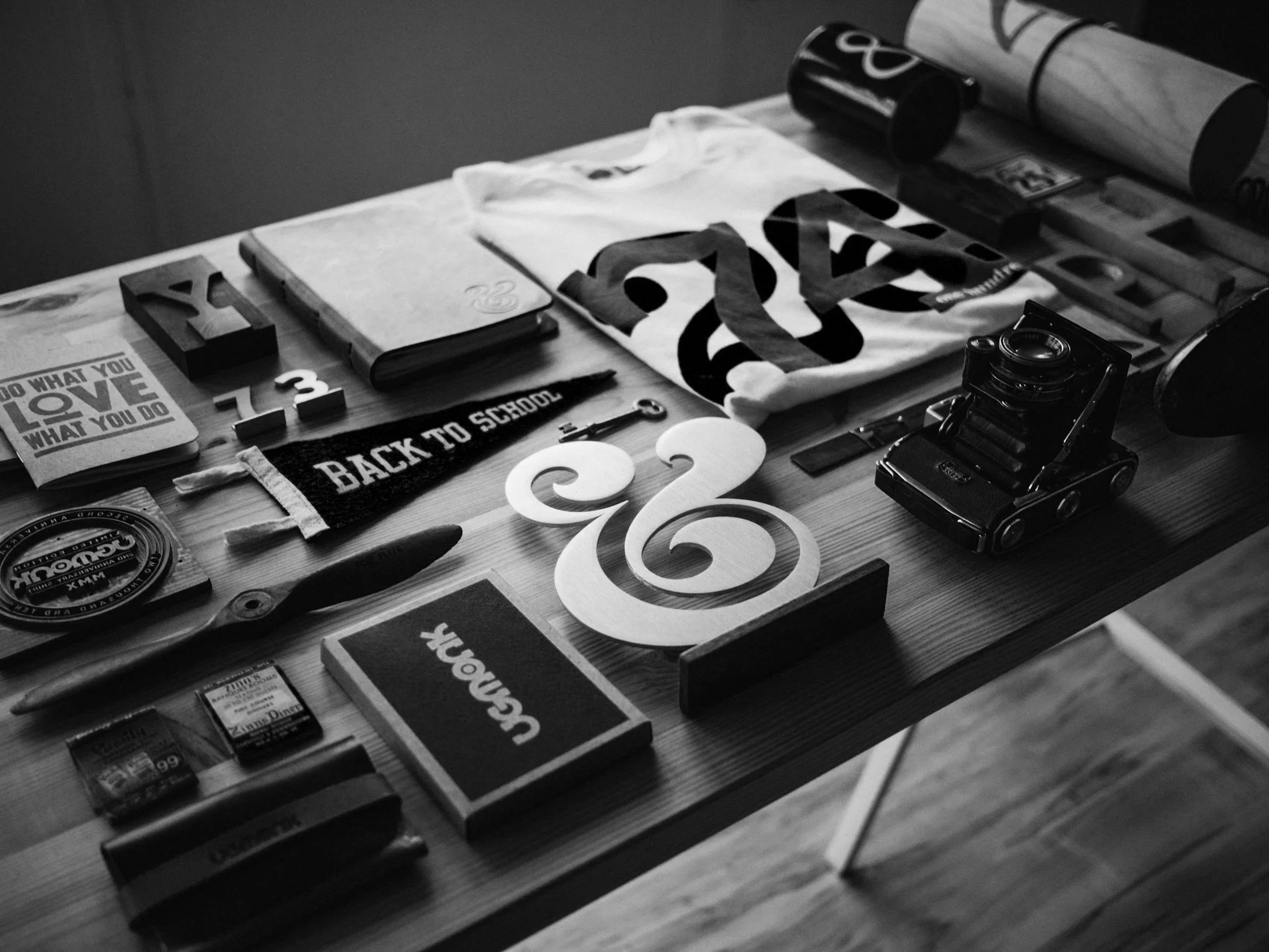 A table with various items including a notebook, cut-out letters, a canvas with the word 'LOVE,' small containers of snacks or pills, a poster with the hashtag '#vlog,' and a toy car.