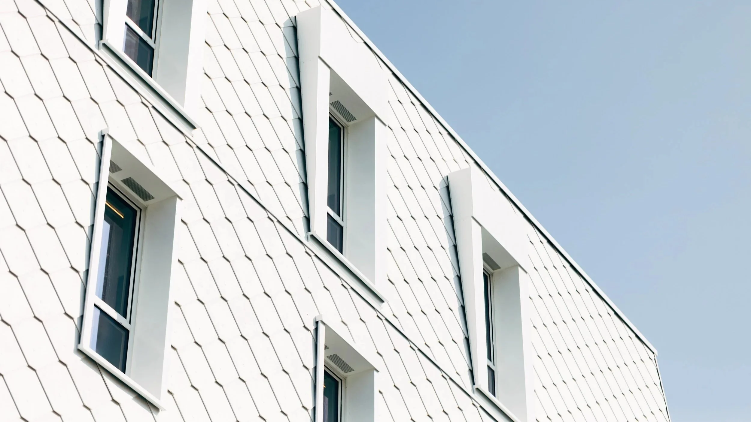 Modern white building with vertical, narrow windows and a patterned exterior wall against a clear sky.