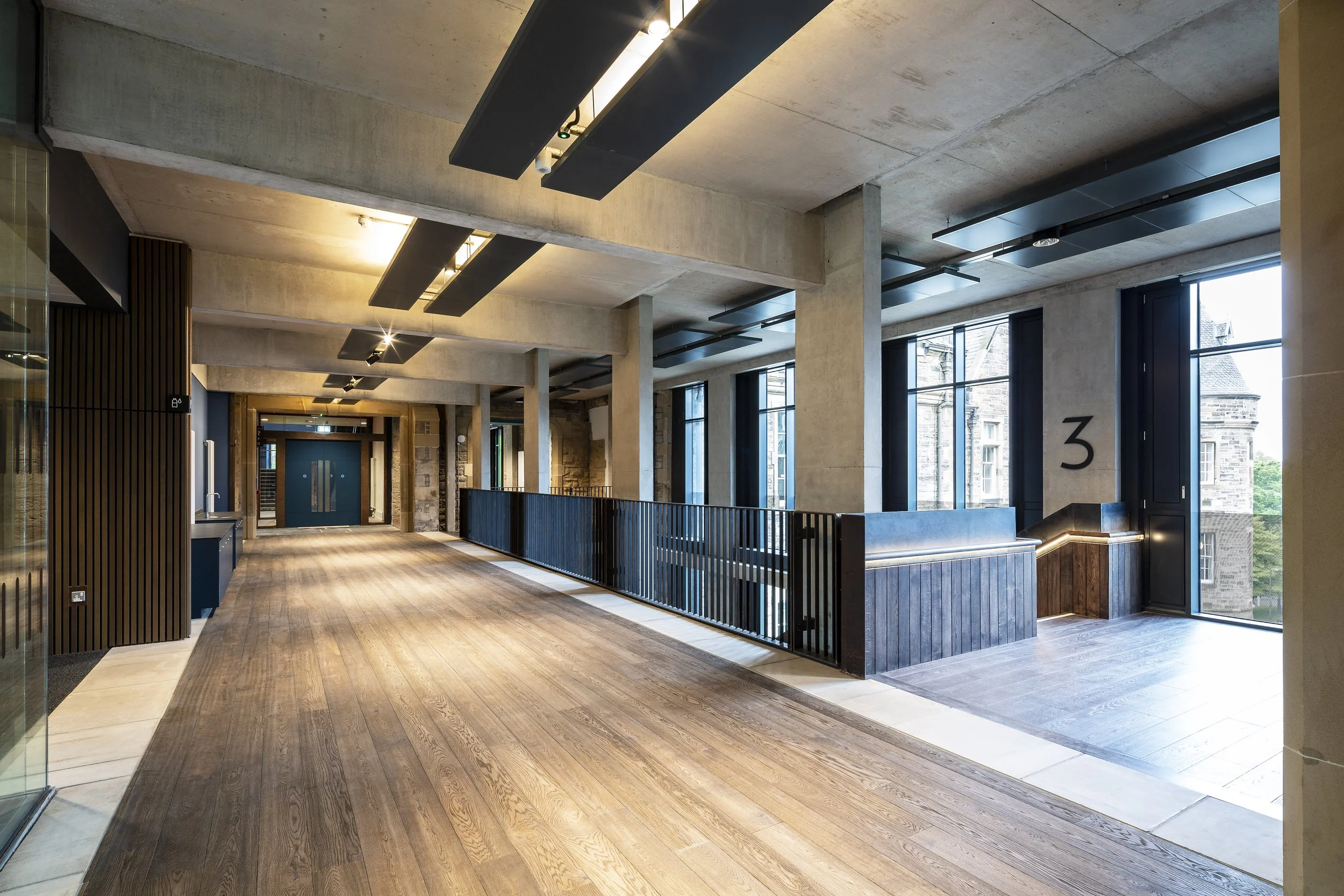 Interior of a modern building with wooden floors, concrete ceilings, large windows, and a staircase leading up near the number 3.