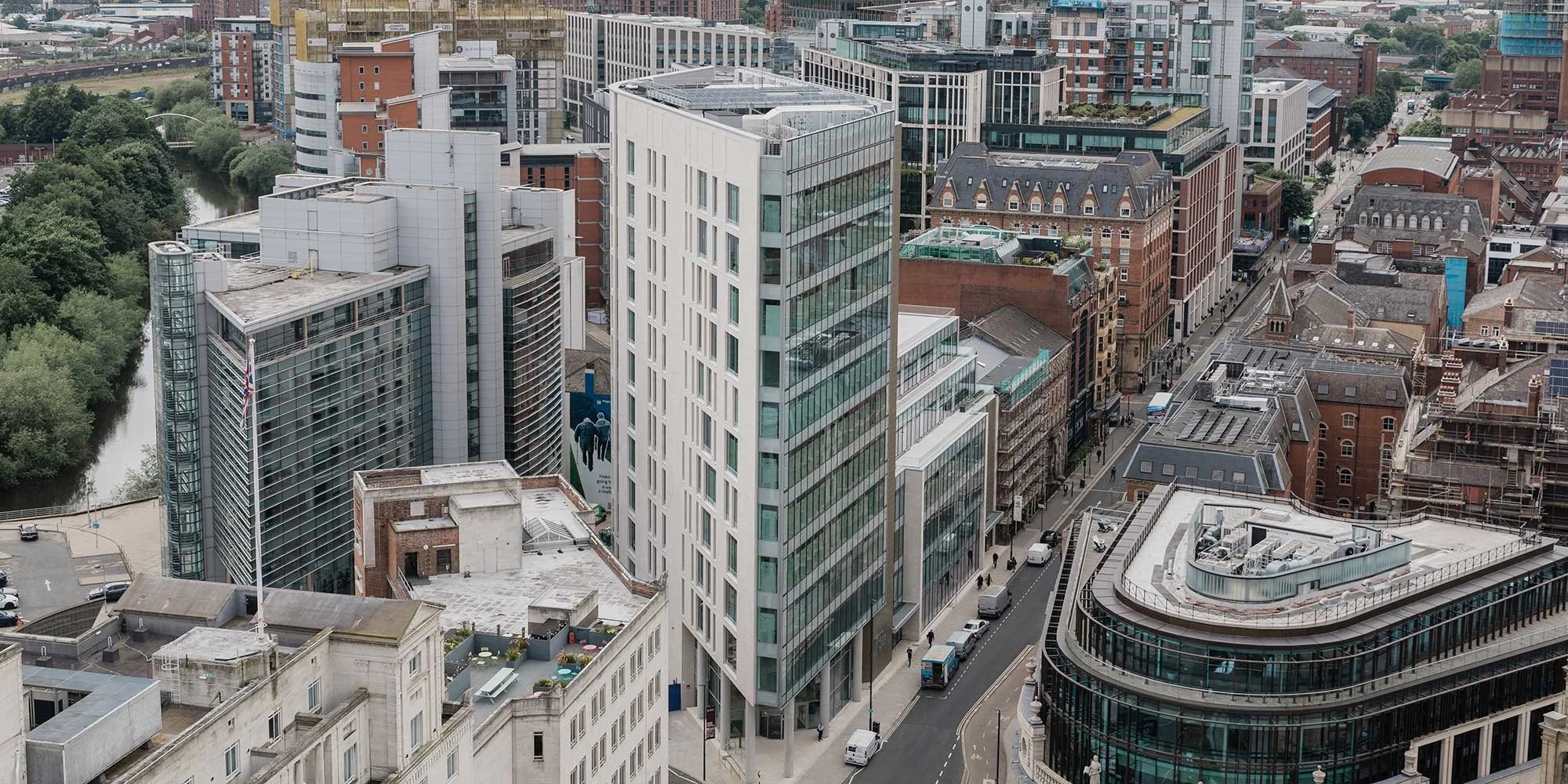 Aerial view of a city featuring high-rise buildings, office towers, and office buildings on the streets surrounded by trees and a river.