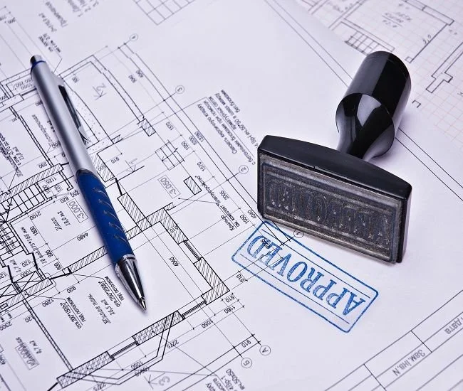 Blueprints of a building, a blue pen, and an approval stamp