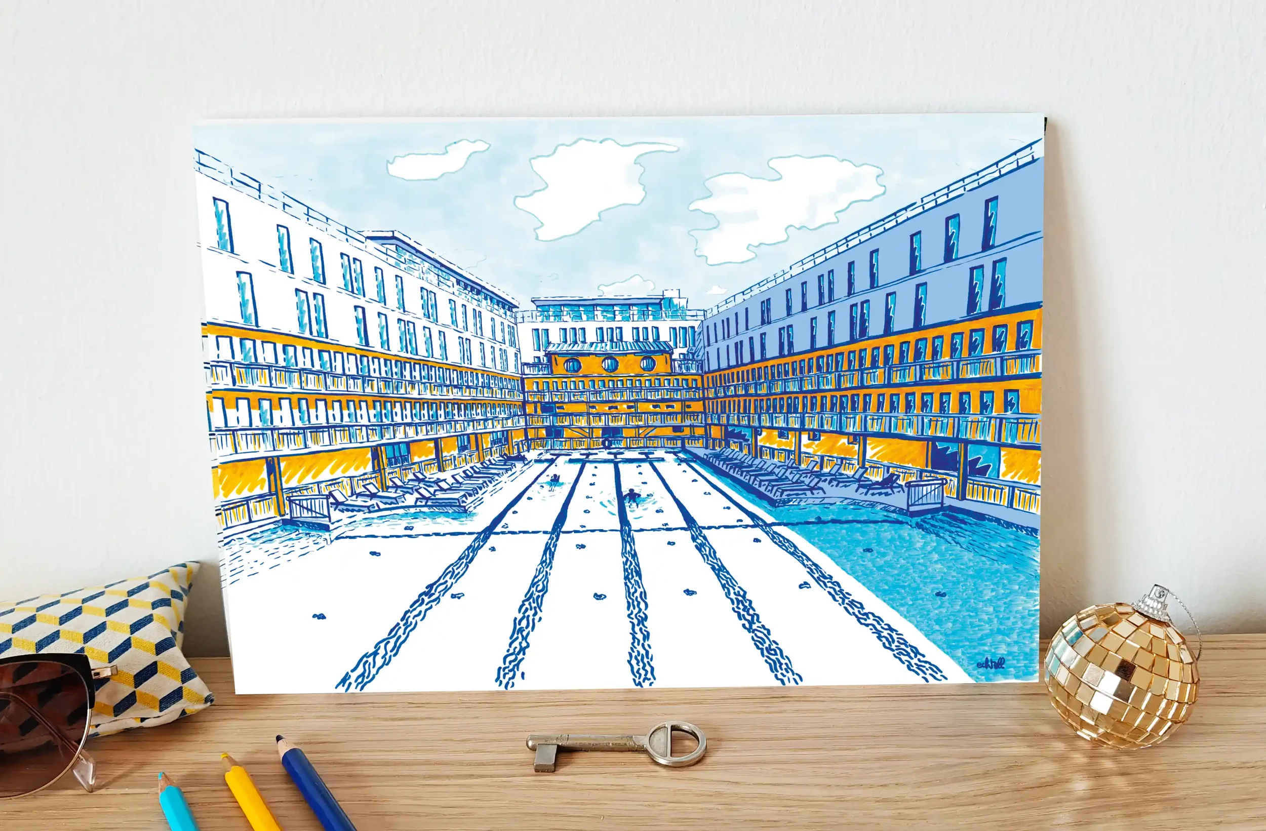 Affiche souvenir de l'hôtel Molitor à Paris posée sur un bureau avec des crayons, des lunettes de soleil, une clé de chambre d'hôtel et une boule disco