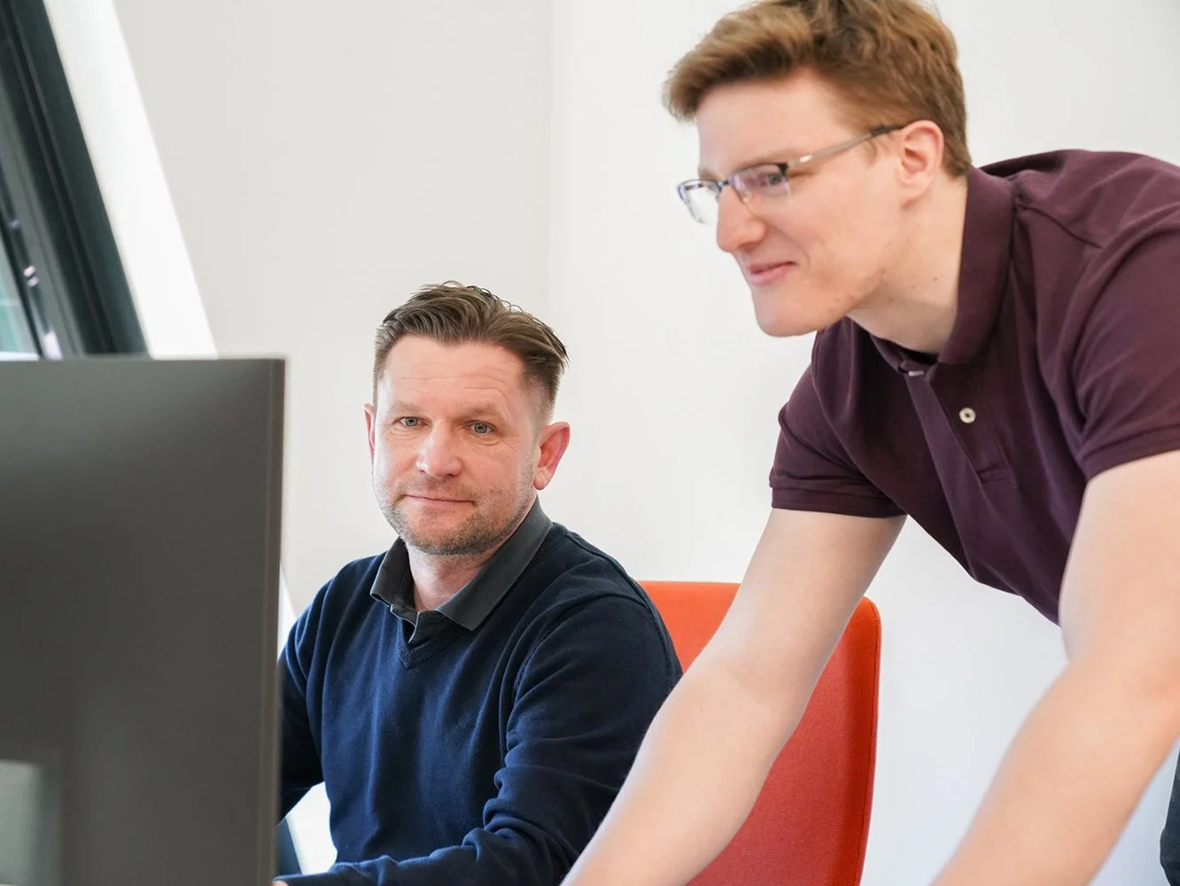 Zwei Männer arbeiten gemeinsam an einem Computer im Büro.