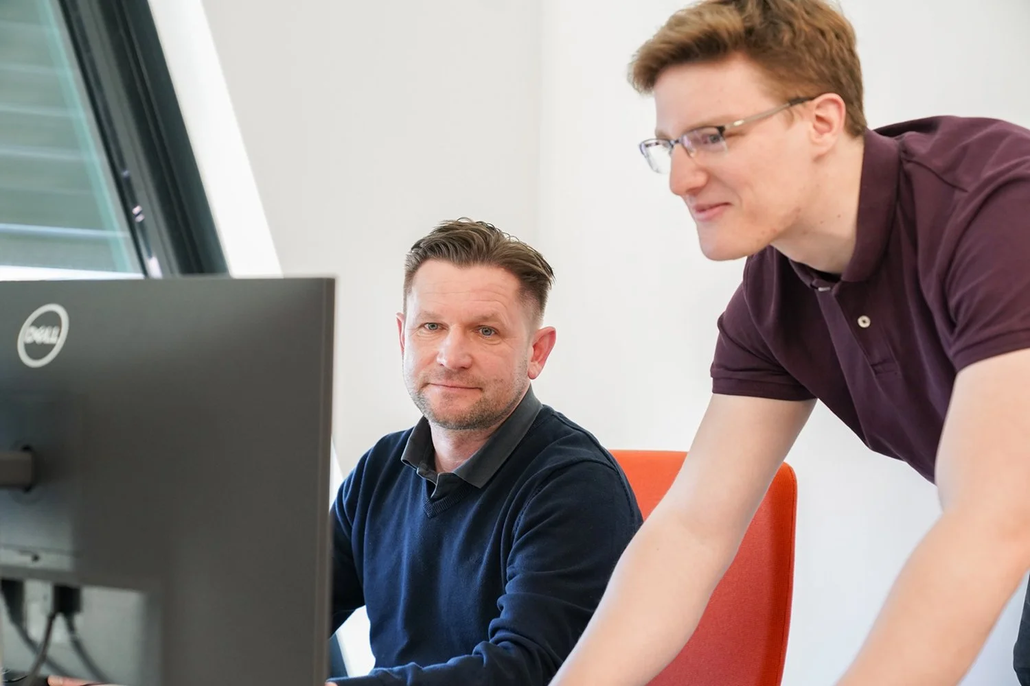 Zwei Männer arbeiten zusammen vor einem Computer in einem Büro.