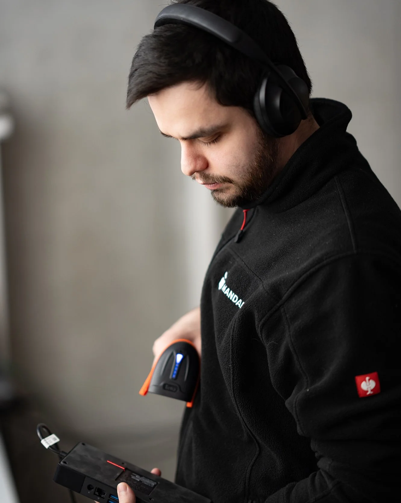 Mann in schwarzem Pullover mit Firmenlogo, trägt schwarze Kopfhörer und hält ein mobiles Lesegerät, das eine elektronische Karte scannt.