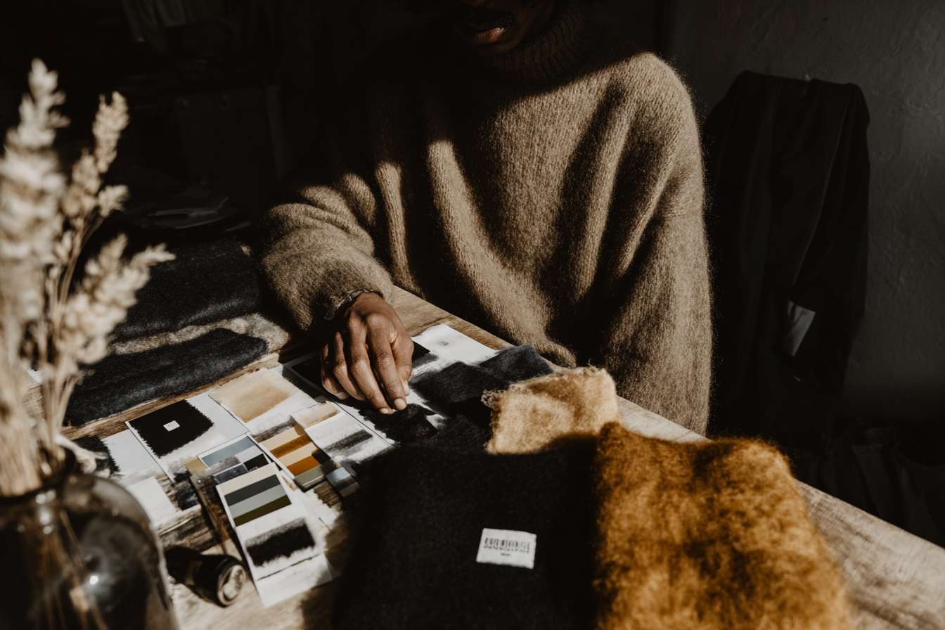 Atelier-Detail: Frauenhand mit Stoffmustern und Farbkonzepten am Schreibtisch – Consulting bei Studio ARTVÉA