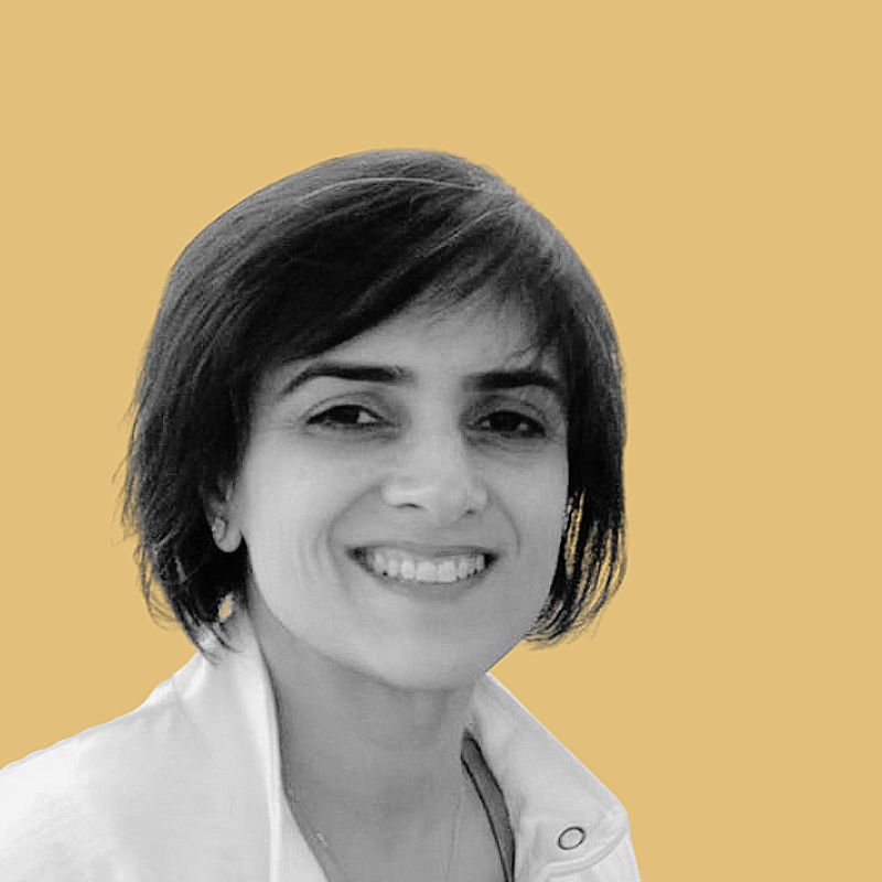Black and white portrait of a smiling woman with short hair, wearing a collared shirt, against a solid light brown background.
