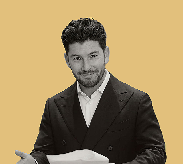 Black and white photo of a man in a suit, smiling in profile, holding a cleaning cloth against his face, against a solid light yellow background.