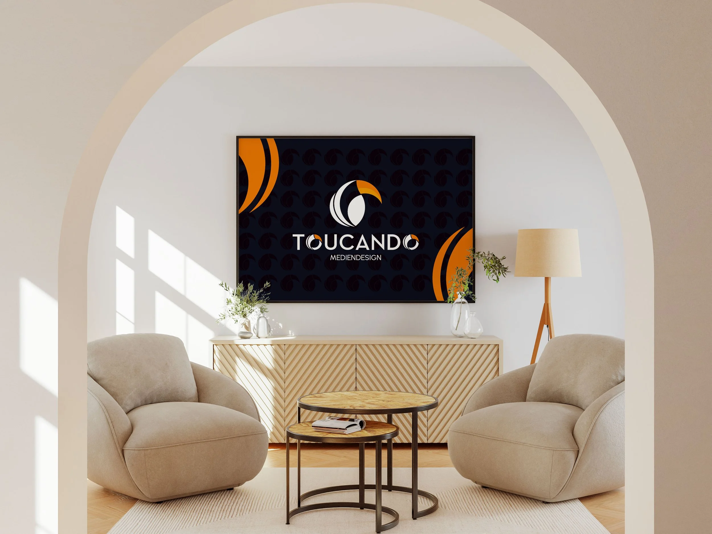 Modernes Wohnzimmer mit zwei beigen Sessel, einem runden Couchtisch, einem weißen Sideboard mit Pflanzen und einer Stehlampe, auf der einen Wand hängt ein schwarzes Bild mit einem Logo und der Aufschrift 'TOUCANDO MEDIENDESIGN'.