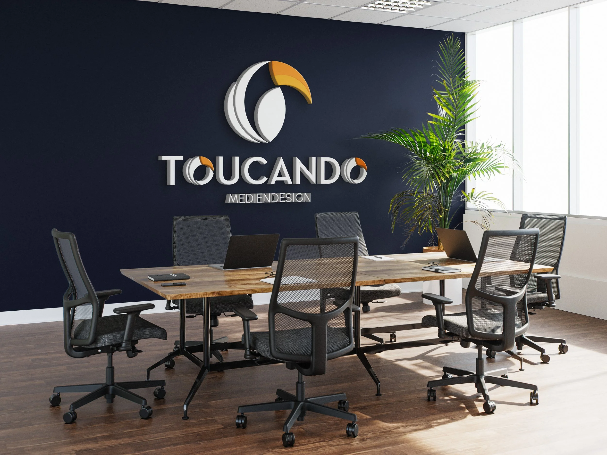 Modernes Konferenzzimmer mit sechs Stühlen, einem Holztisch, Laptops, Notizbüchern, und einem großen Firmenlogo an der dunklen Wand, bestehend aus einem stilisierten Vogelkopf und dem Text "TOUCANDO MEDIENDESIGN".