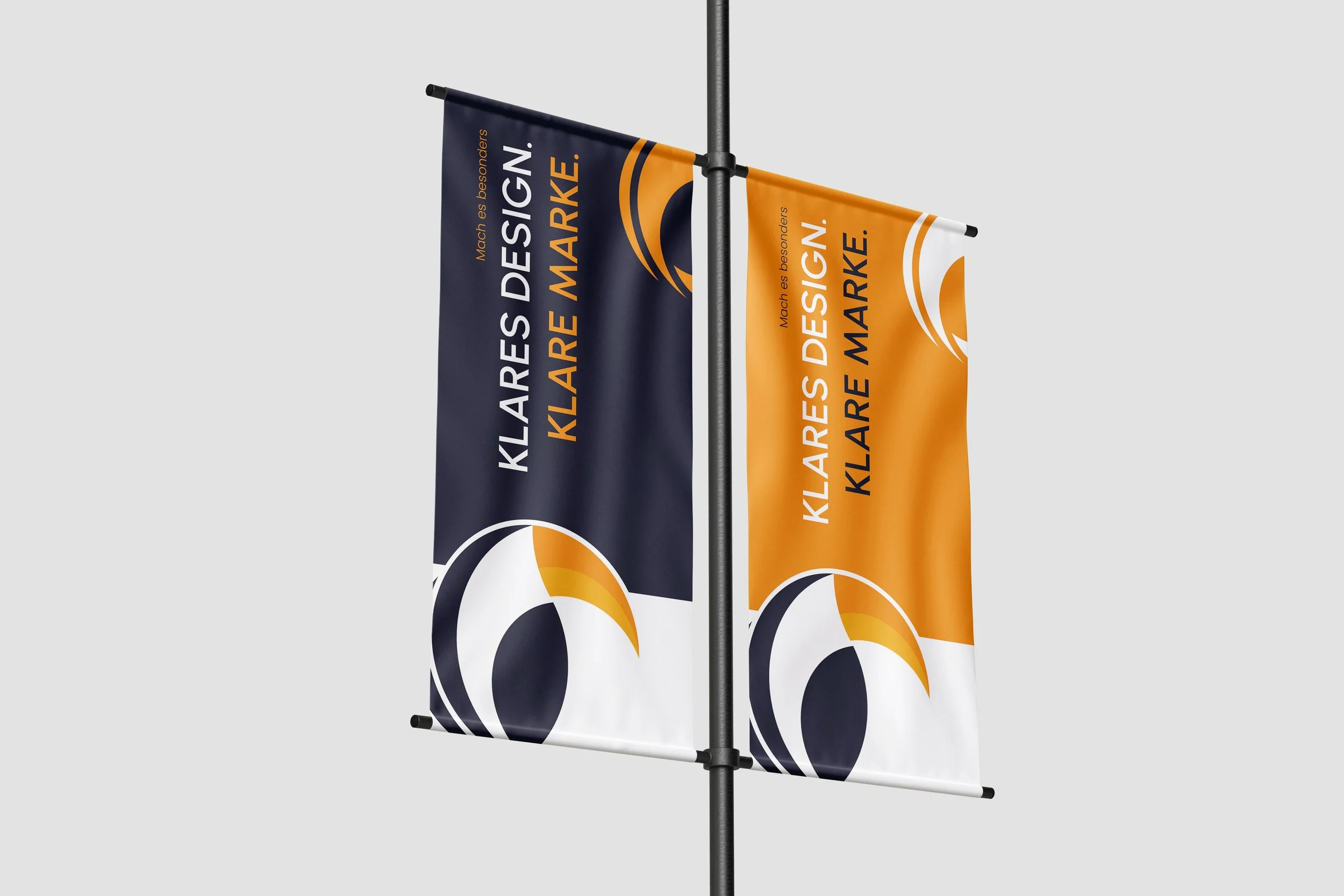 Zwei Werbefahnen auf einem Mast, die Werbung für klares Design machen. Eine Fahne ist dunkelblau und die andere orange, beide zeigen einen stilisierten Vogelkopf und den Text in Deutsch.