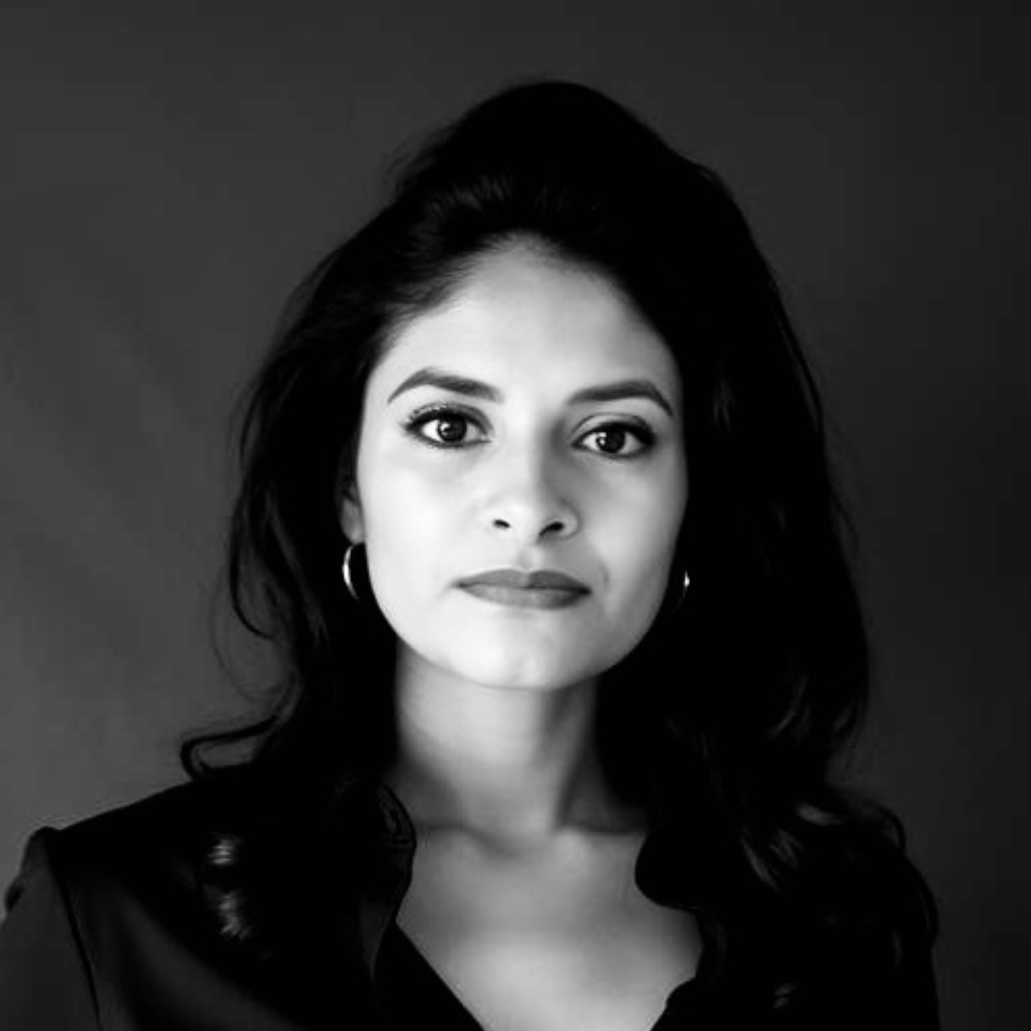 Black and white portrait of a woman with dark, wavy hair, wearing hoop earrings, and looking directly at the camera.