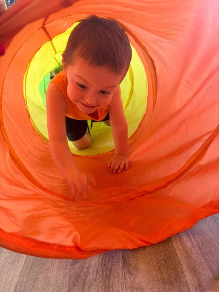 A young boy crawling through a colorful, tunnel-shaped play tent, smiling and having fun.