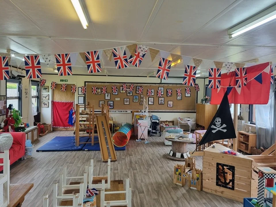 A children's playroom decorated with British flags and pirate-themed decorations for a celebration, featuring toys, furniture, and play equipment.