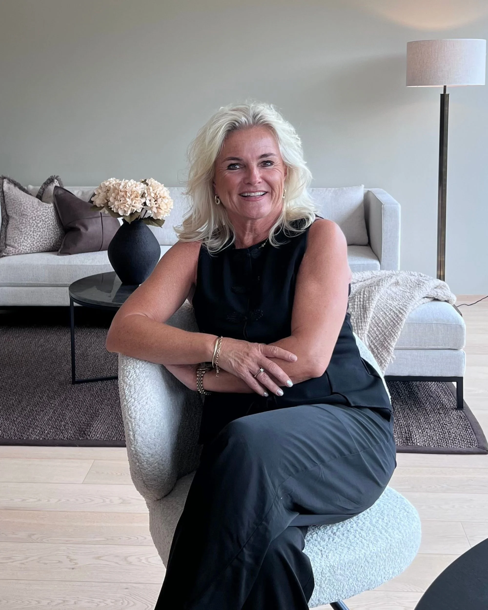 Bilde av en smilende innehaver av Ellen Hagen boligstyling/ interiørdesign som  sitter i en stol i leilighet stylet hos kunde.