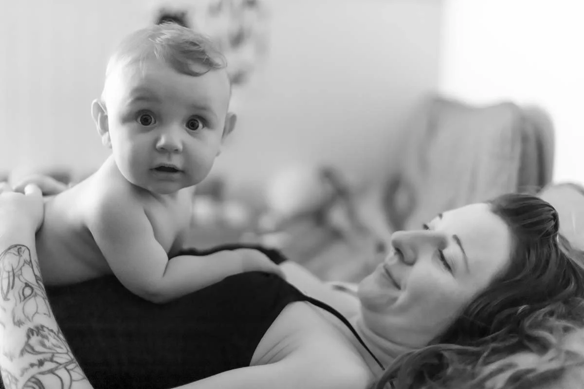A baby and woman lying on a couch, the baby looking surprised and the woman smiling.