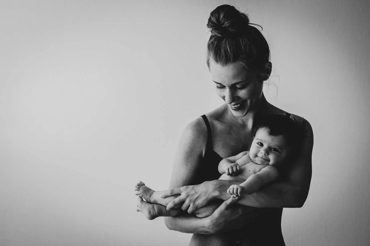 A woman holding a baby and smiling while looking at the baby.
