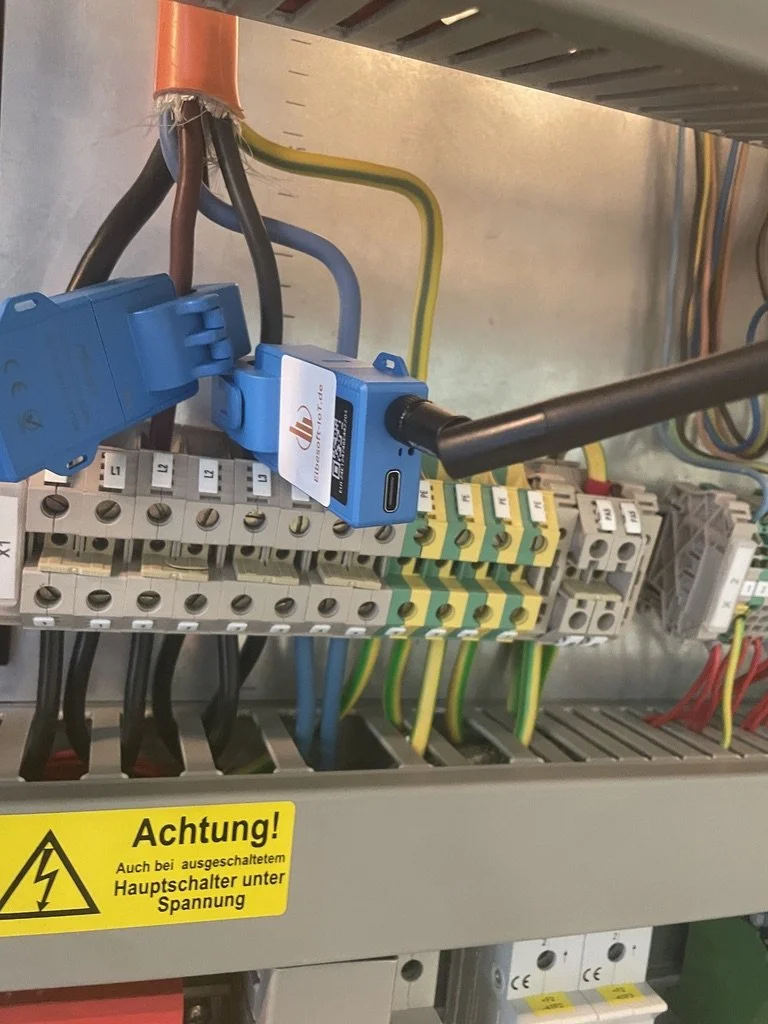 Elektrischer Schaltschrank mit mehreren kabellosen Messgeräten, gelber Sicherheitsaufkleber und verschiedene farbige Drähte.