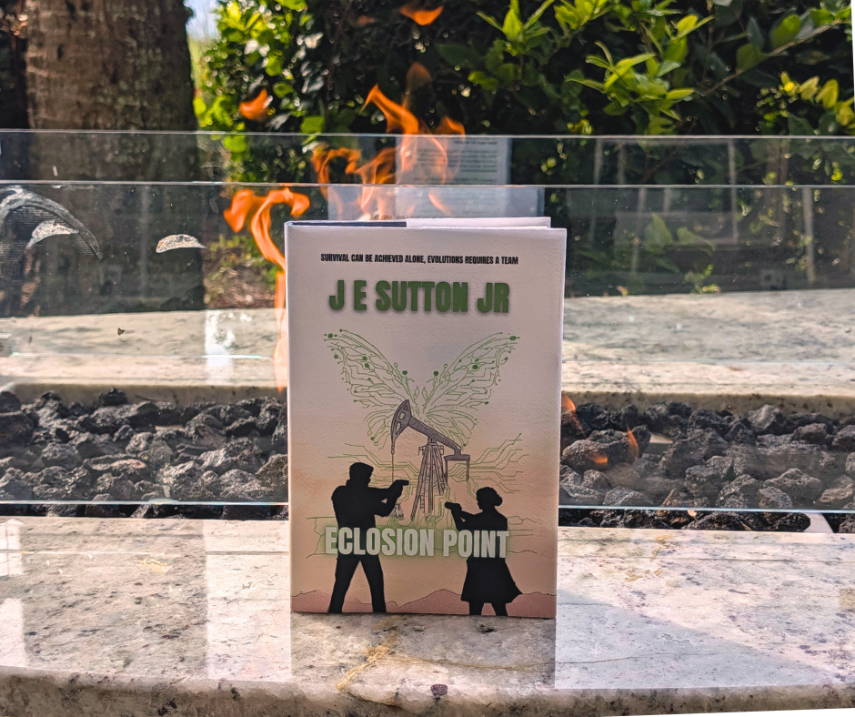A book titled 'Eclosure Point' by J E Sutton Jr stands upright in front of an outdoor fireplace with visible flames. Two silhouettes, a man and a girl, are illustrated on the cover, appearing to interact or observe an oil pumpjack with digital circuit lines and butterfly wings above it. The background features a garden with greenery and trees.