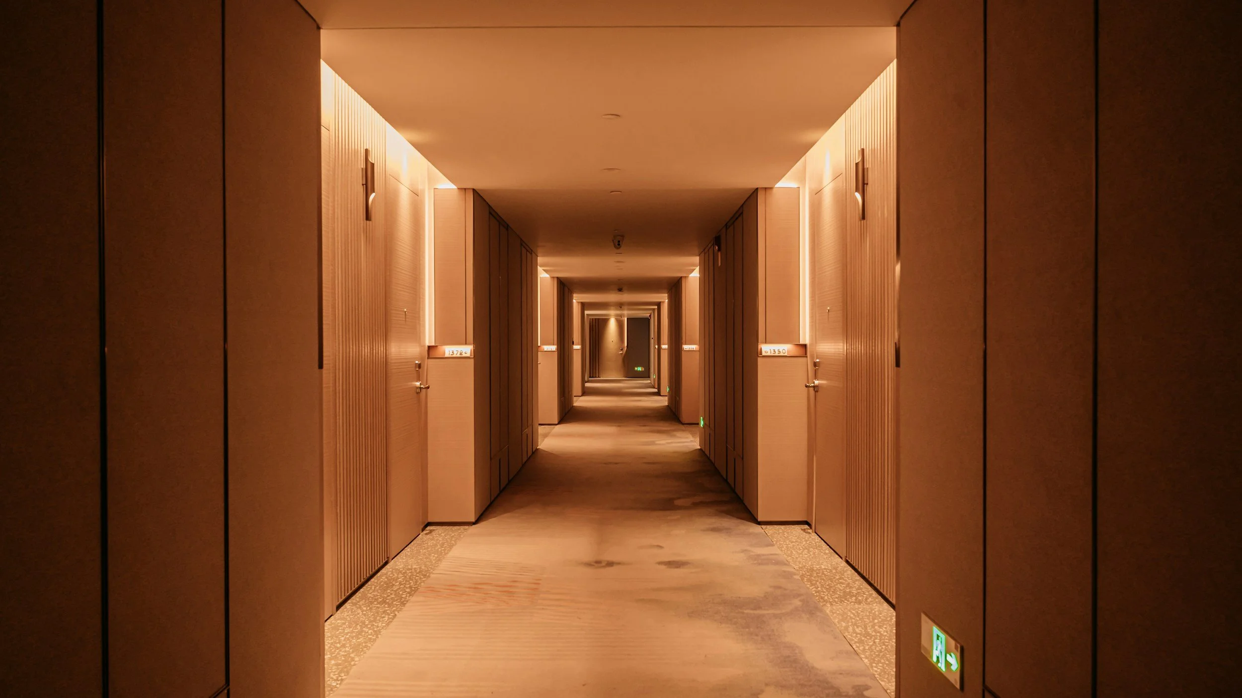 Lange, lege hotelgang met zachte verlichting en gesloten deuren aan beide zijden.