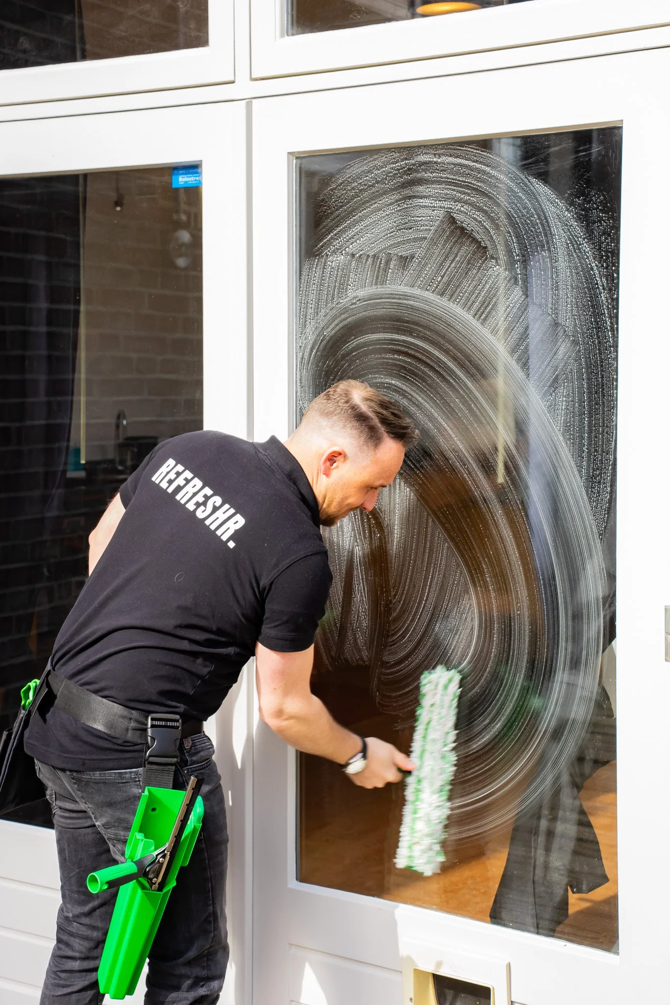 Man die het raam van een deur bijwerkt met een schoonmaakborstel, terwijl de ruit bedekt is met zeepschuim.