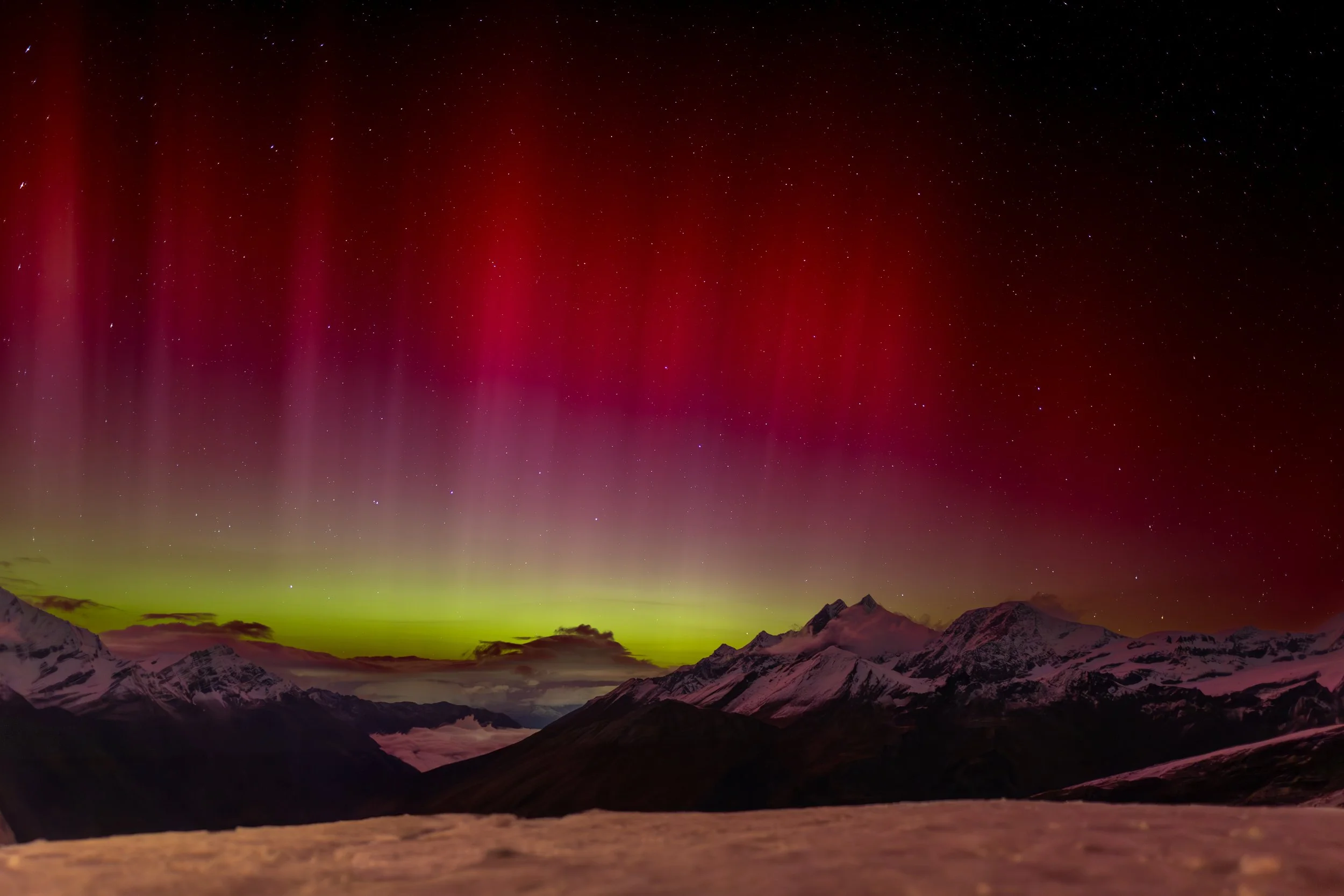 Northern lights (aurora borealis) glowing red and green in the night sky above snow-capped mountains.