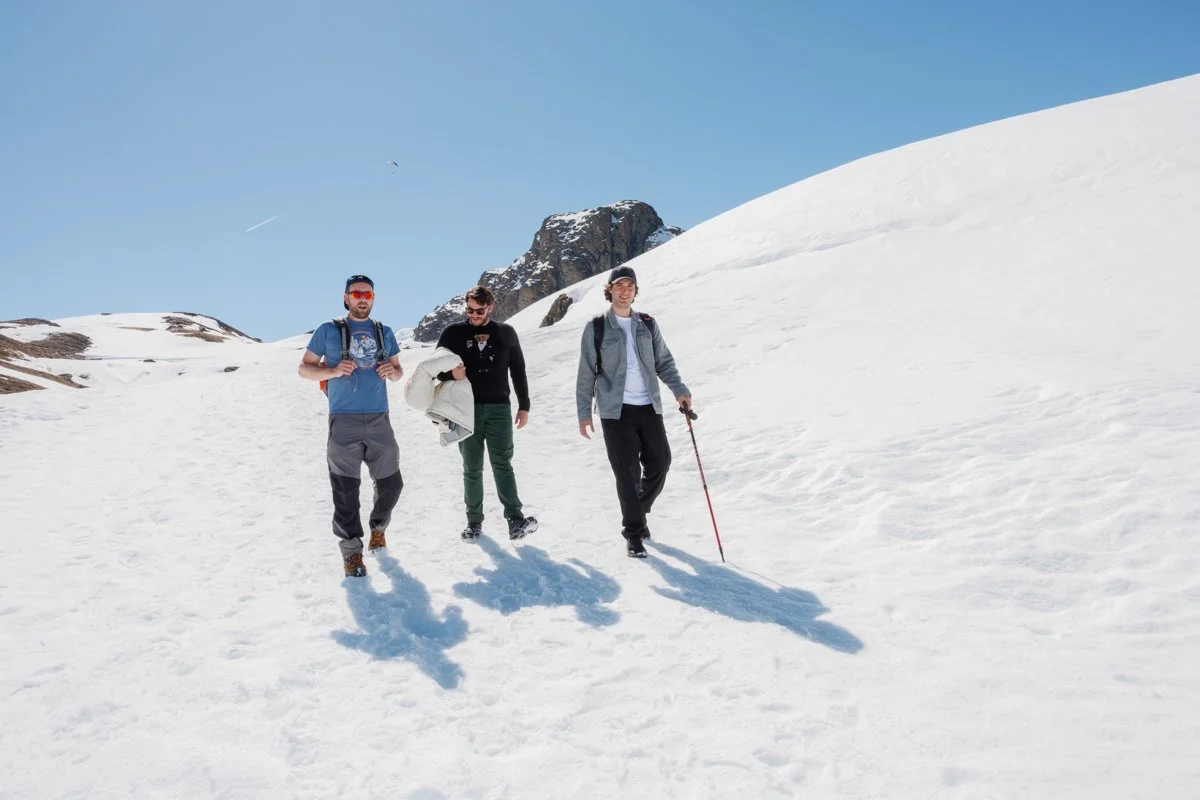 Three men hiking in a snow-covered mountainous area on a clear, sunny day.