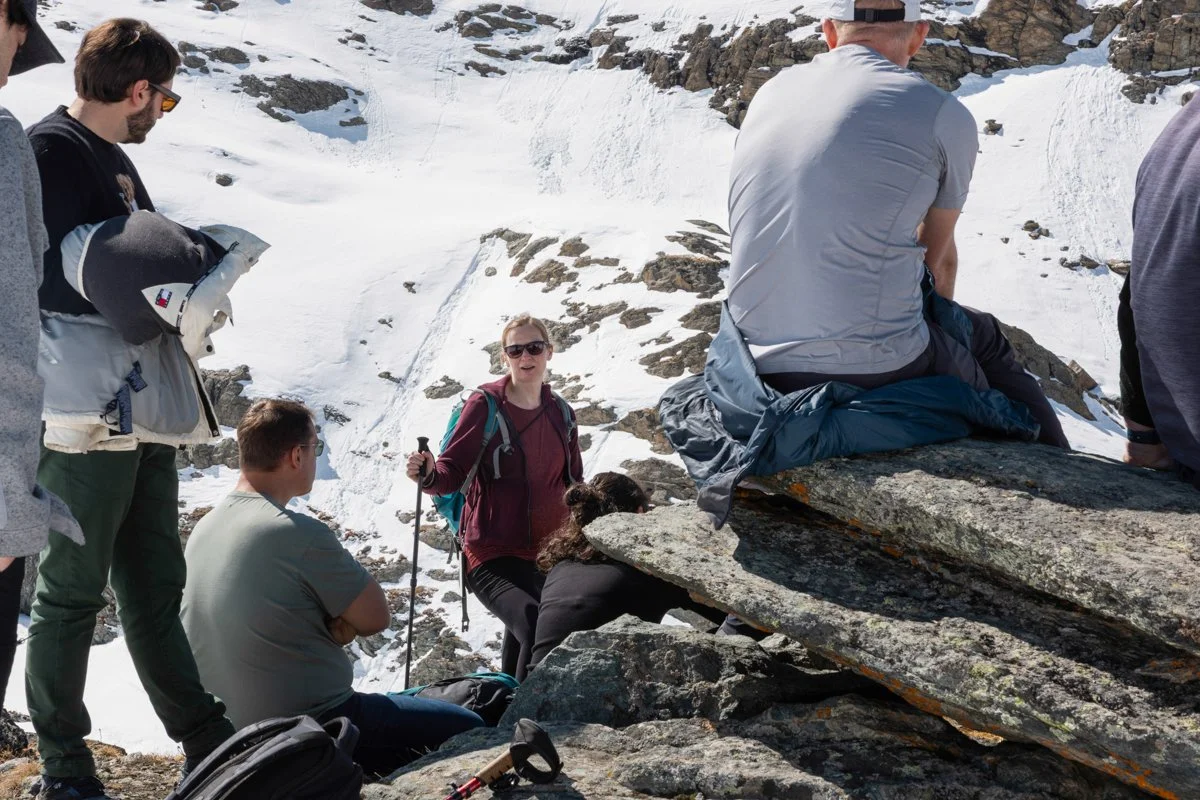 Group of hikers resting on rocky terrain with snow-covered mountains in the background
