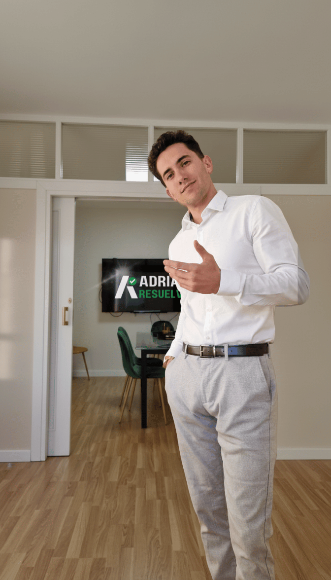 Hombre con camisa blanca y pantalones grises en una oficina, señalando hacia la cámara, con pantalla que dice 'Adriana Resuelta' en el fondo.