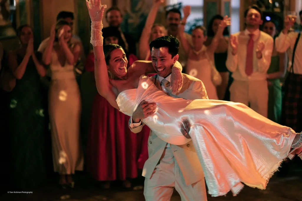 A bride and groom dancing at their wedding reception, with guests clapping in the background.