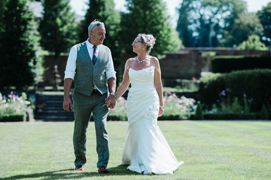 A bride and groom holding hands and walking on a grassy lawn during a wedding celebration outdoors.