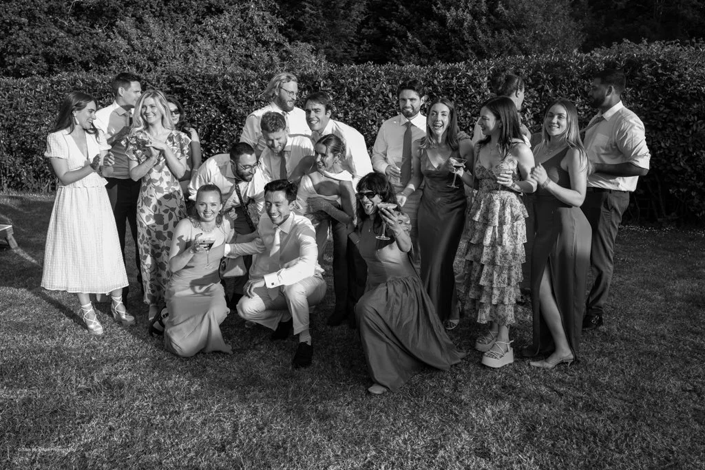 Group of people dressed in formal attire outdoors, posing and enjoying drinks at a gathering or celebration.